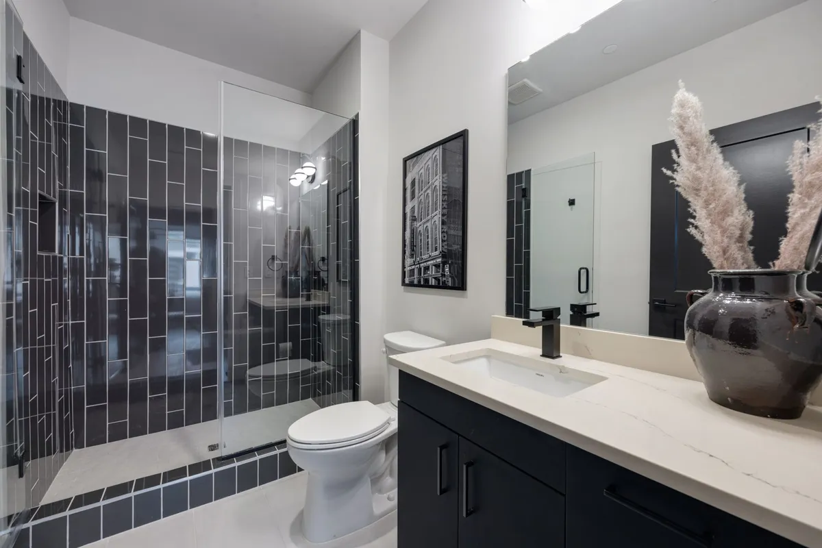 A contemporary bathroom featuring a glass-enclosed standing shower, dark cabinetry, a decorative vase with pampas grass, and framed wall art. The space feels modern, spacious, and spa-like—ideal for unwinding after a day in the city.