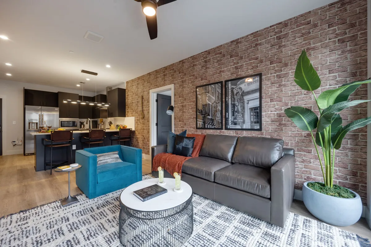 A stylish, sunlit living and dining area featuring a plush blue chair, modern sofa, designer artwork, and a chic dining table—all arranged for comfort and socializing in a contemporary Nashville home.